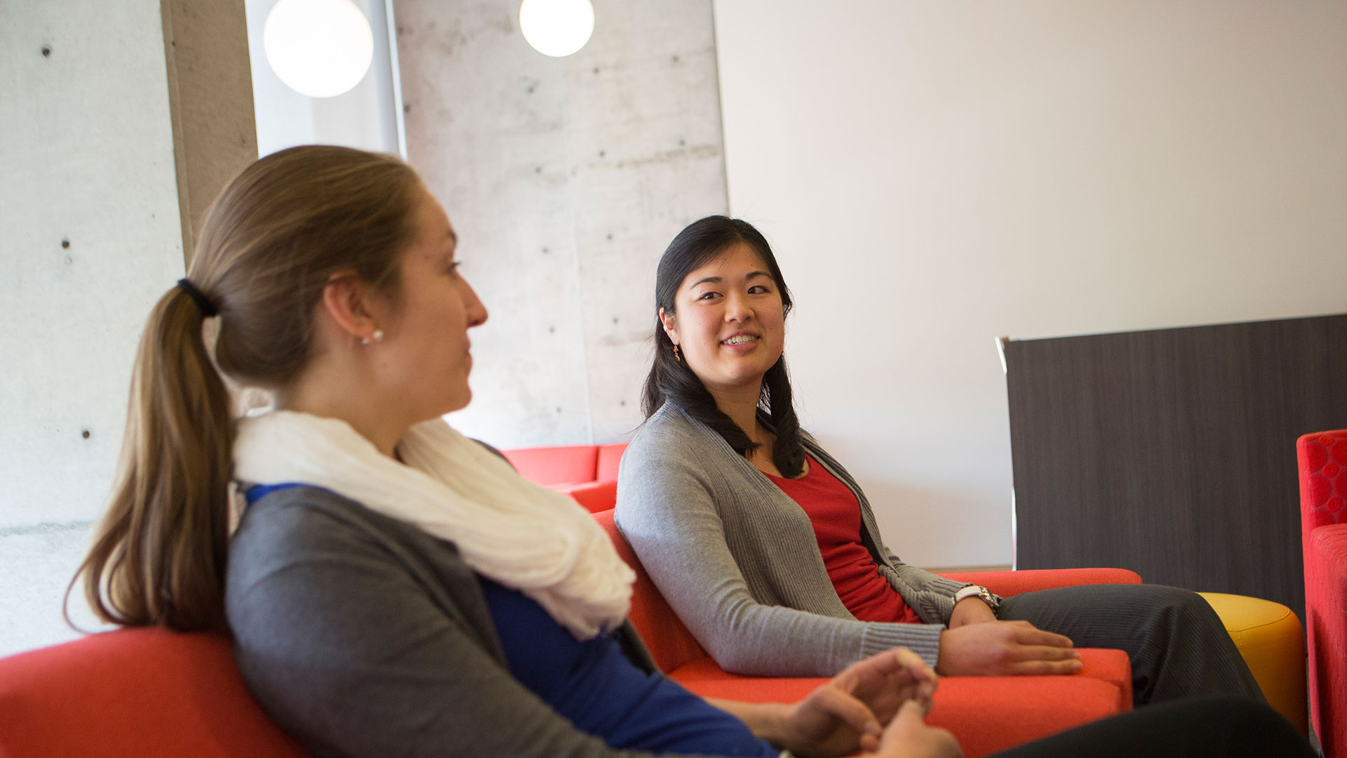 Two women talk in red chairs