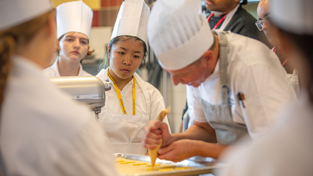 Students watch as a professor instructs them on how to prepare pastries