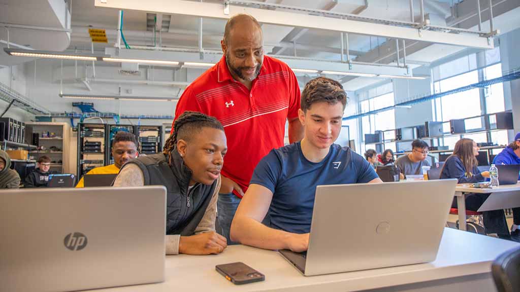 Professor Anthony Chavis works with two male students in the Network Engineering Lab.