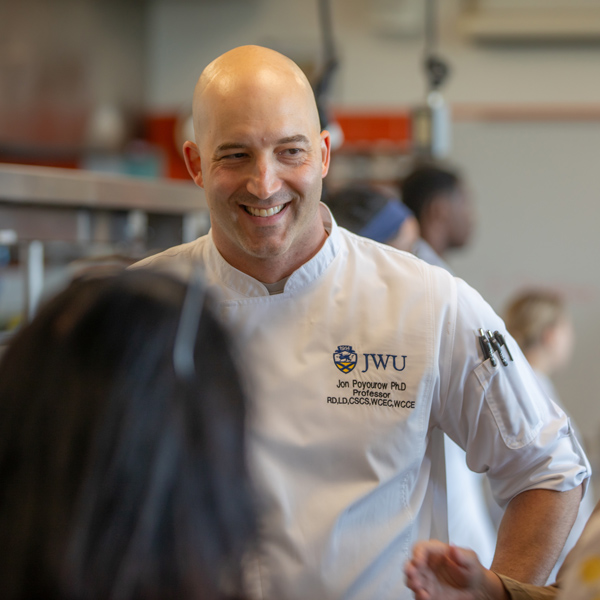 a photo of Chef Jonathan Poyourow smiling as he addresses a student in the kitchen