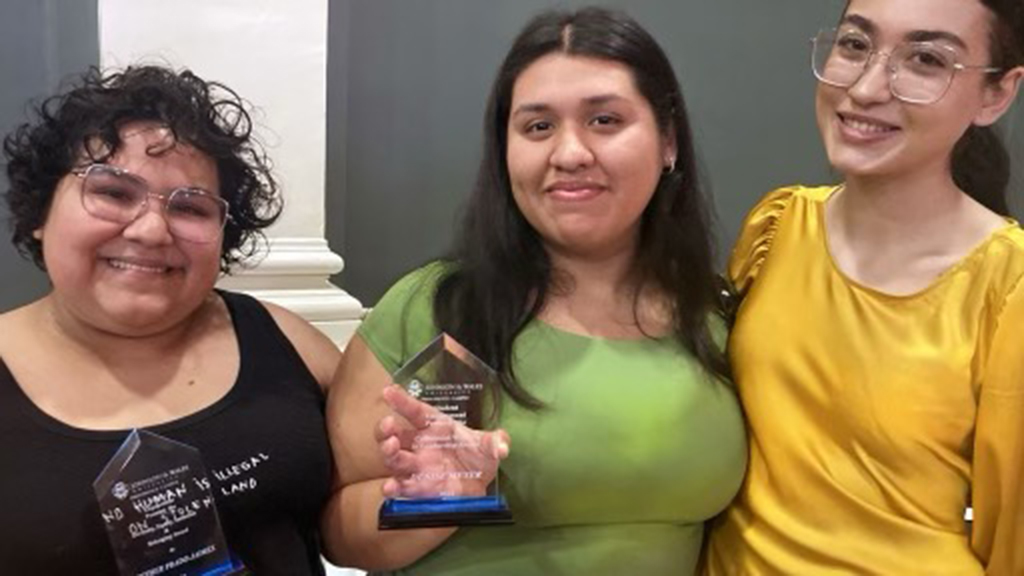 Three students smiling with trophies.