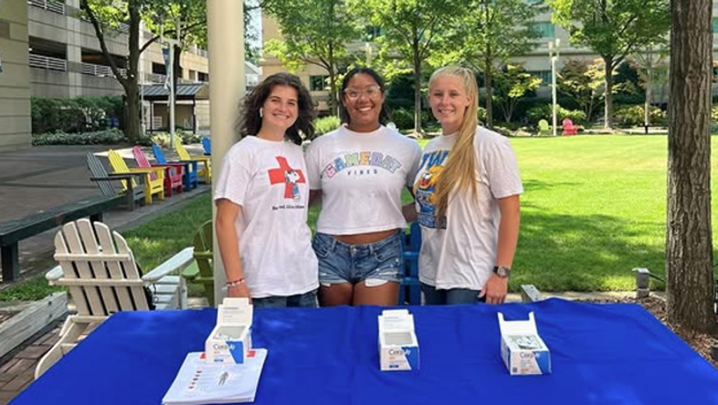 three female students pose at a table promoting the HOSA student club