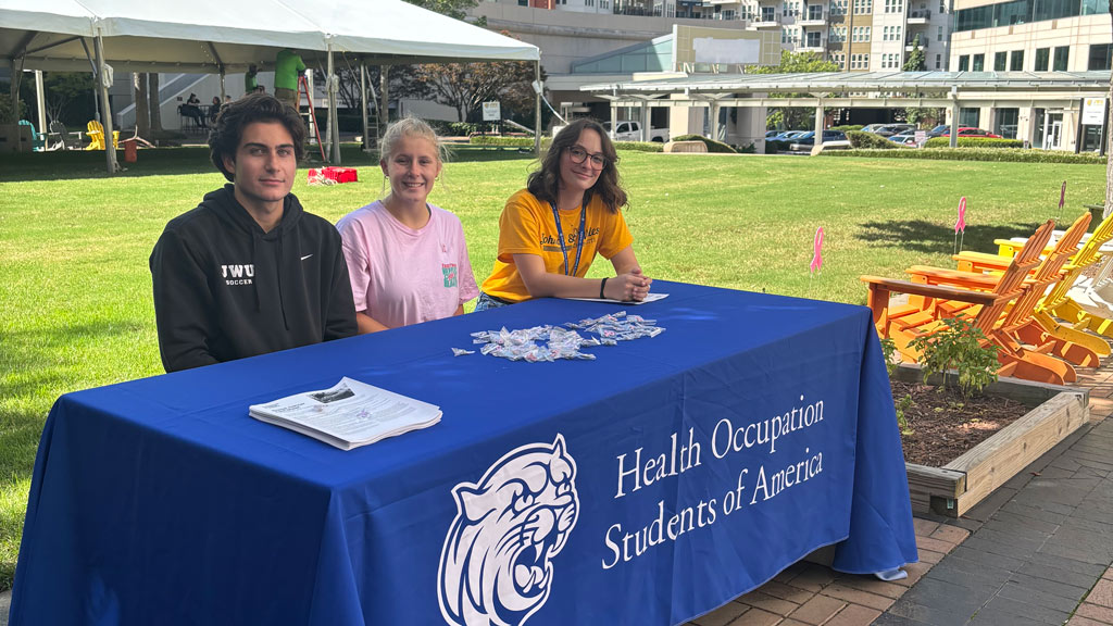 three students sitting at a table promoting the HOSA student club